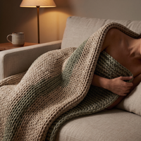 Woman resting under the knit weighted blanket on a linen sofa at dusk