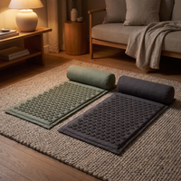 One sage and one charcoal acupressure mat with matching bolster pillows laid out side by side on a wool rug