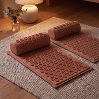 Two terracotta acupressure mats with their bolster pillows laid out side by side on a wool rug in warm lamplight