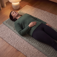 Woman lying flat on her back on the sage acupressure mat, head and whole back resting on the mat, hands settled on her stomach